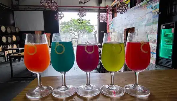 Taças coloridas de chope artesanal alinhadas no balcão da Joy Project Brewing, com decoração da fábrica ao fundo