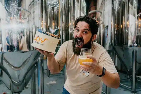 Homem sorridente segurando bolo e copo de chope na fábrica Joy Project Brewing